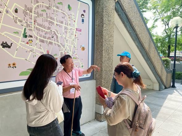 導覽志工在戶外地圖前，與遊客交流田尾旅遊資訊。